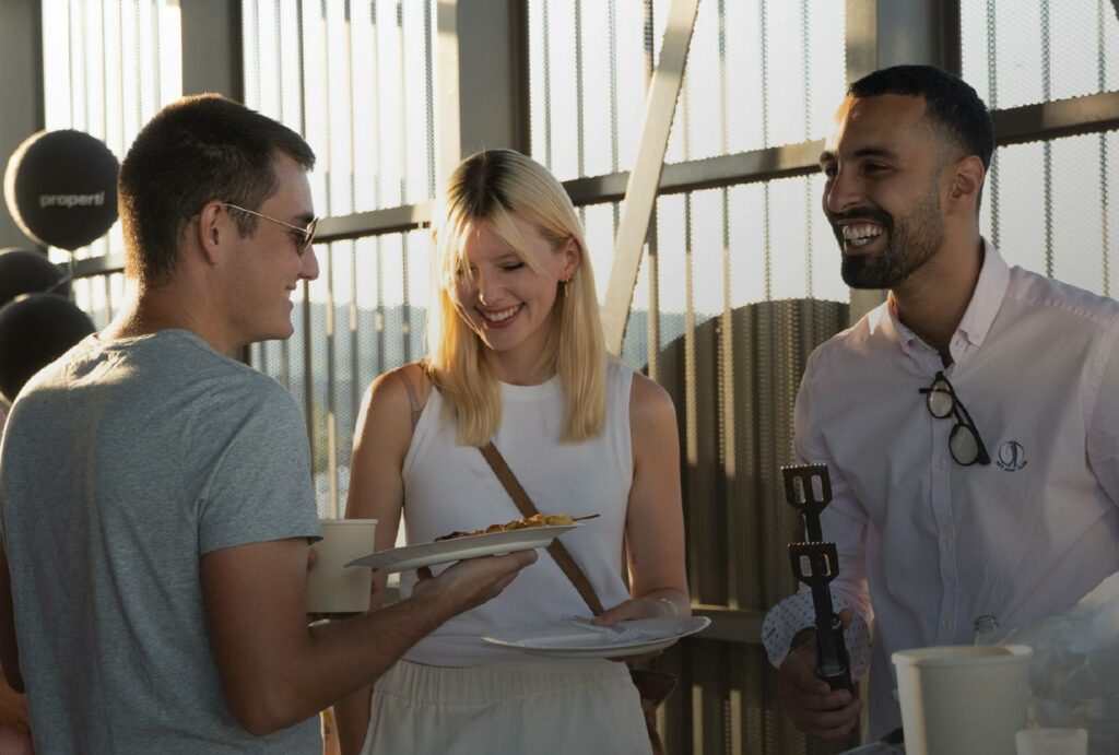 Weibliche und zwei männliche Mitarbeiter von Properti lachen gemeinsam auf der Terrasse am Firmenanlass Rocket Friday
