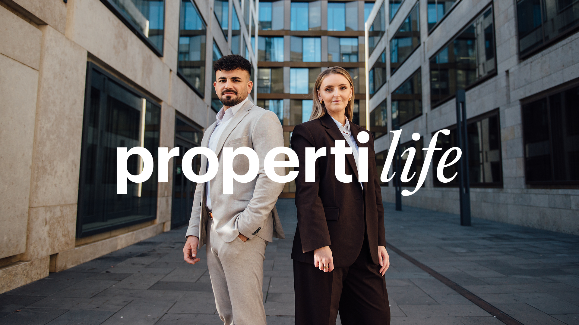 Due agenti immobiliari properti sono in piedi tra immobili moderni e guardano direttamente in camera, sopra di loro la scritta propertilife, il movimento fvon properti per le carriere